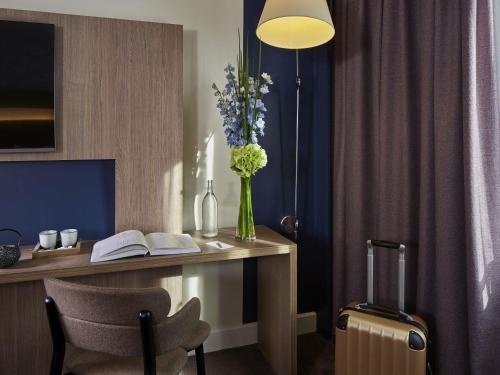 a desk with a vase of flowers and a suitcase at Novotel Paris Les Halles in Paris