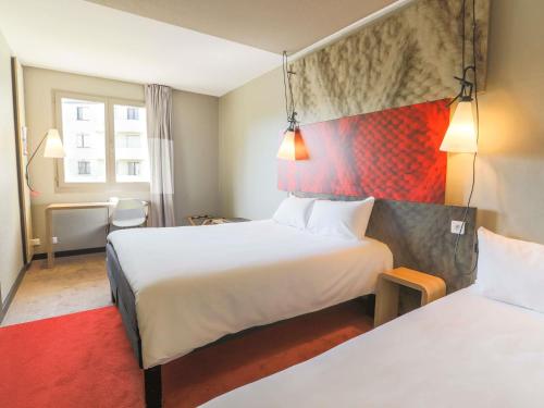 a hotel room with two beds and a red rug at Ibis Saint Étienne - La Terrasse in Saint-Étienne
