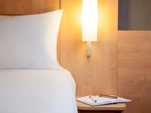 a bed with a lamp and a book on a table at ibis Maine Montparnasse in Paris