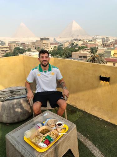 a man sitting on a balcony with a tray of food at Eyad Pyramids view in Cairo