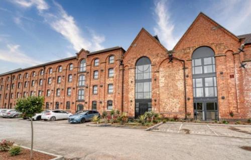 a large brick building with cars parked in a parking lot at Stay at 52 The Maltings, Burton on Trent - Modern One Bedroom Apartment in Burton upon Trent