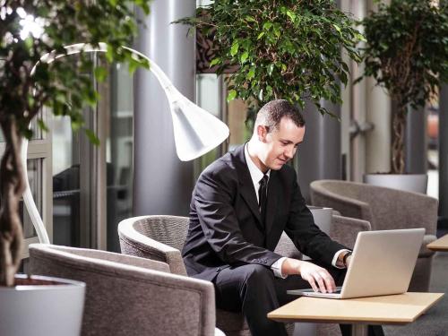 a man sitting in a chair using a laptop computer at Novotel Gent Centrum in Ghent