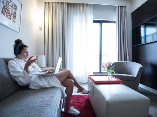 a woman sitting on a couch with a laptop at Novotel Athens in Athens