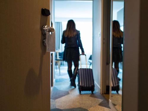 a woman walking down a hallway with her luggage at Mercure Lorient Centre in Lorient