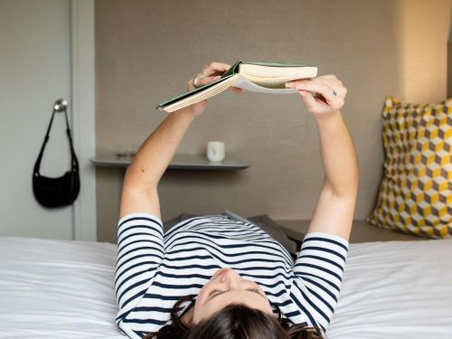 a woman laying on a bed reading a book at ibis Styles Paris Bercy in Paris