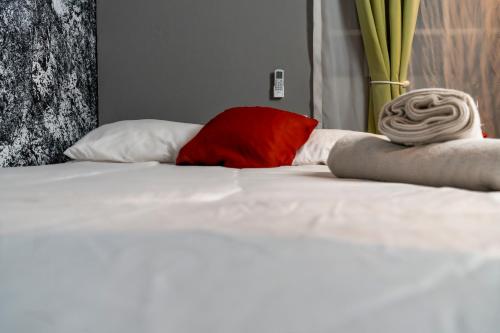 a white bed with a red pillow on it at Gardens House, Airport Juan Santamaría, Alajuela, San José in Alajuela City