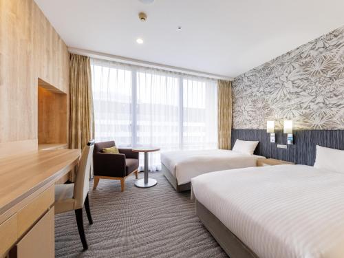 a hotel room with two beds and a desk at Nishitetsu Resort Inn Naha in Naha
