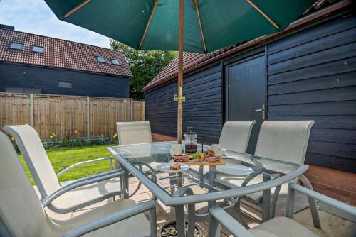 a glass table with chairs and an umbrella on a patio at Sparrows Nest Woodbridge in Martlesham
