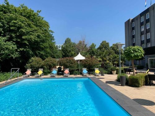 a large swimming pool with chairs and a building at Novotel Maastricht in Maastricht
