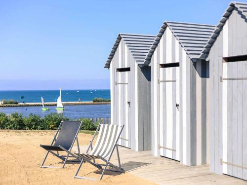 two chairs on a beach with two beach huts at Côte Ouest Thalasso & Spa Les Sables d'Olonne - MGallery Collection in Les Sables-dʼOlonne