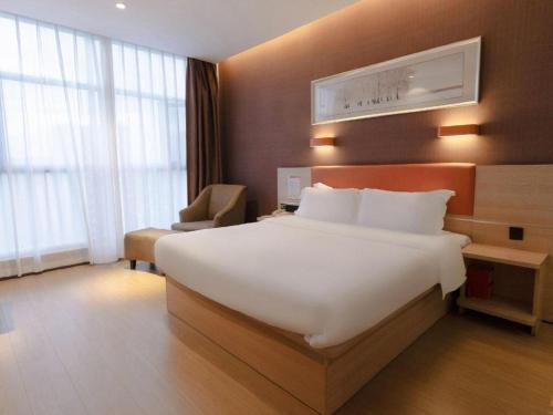 a hotel room with a large white bed and a chair at 7Days Premium Yichang Railway Station East in Yichang
