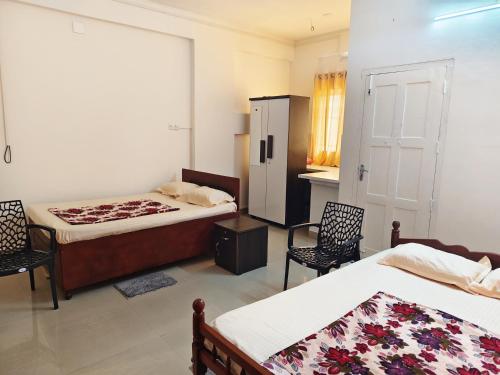a bedroom with two beds and two chairs and a refrigerator at Guruvayurappan Stay, Entire Flat, Near East Nada Guruvayur in Guruvāyūr
