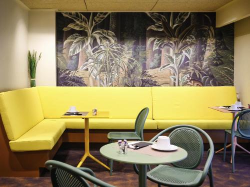 a yellow couch in a restaurant with tables and chairs at Mercure Perpignan Centre in Perpignan
