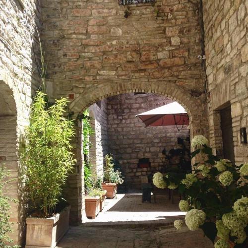a stone archway with a table and an umbrella at Residenza La Corte Assisi in Assisi