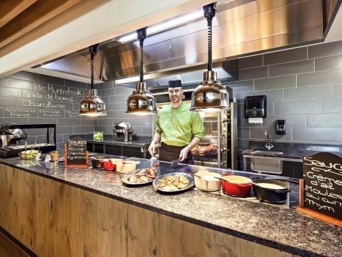 a man standing behind a counter in a kitchen at ibis Site du Futuroscope in Chasseneuil-du-Poitou