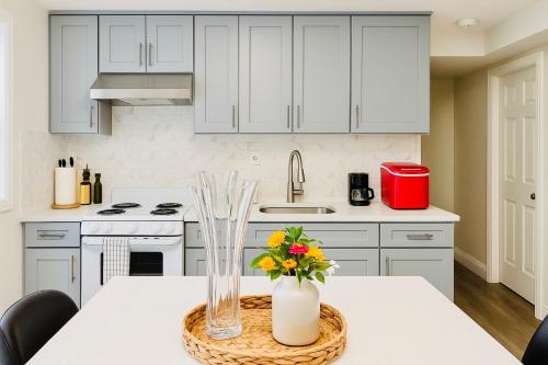 a kitchen with white cabinets and a table with flowers in a vase at Comfort Stay by Stony Brook University & Hospital in Centereach