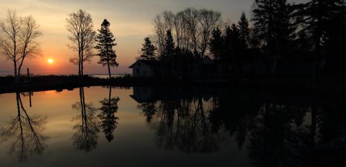 a sunset over a lake with trees and a house at Auberge La Coudriere (Cool Hotel) in L'Isle-aux-Coudres