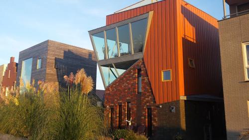 an orange building with a glass facade next to two buildings at Casa Mirador Sleep Inn in Almere