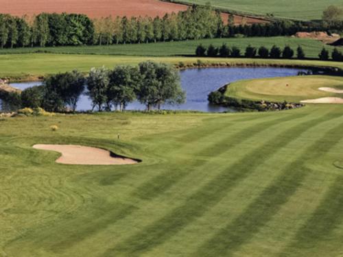 an aerial view of a golf course with a pond at Mercure Bayeux Omaha Beach in Port-en-Bessin-Huppain