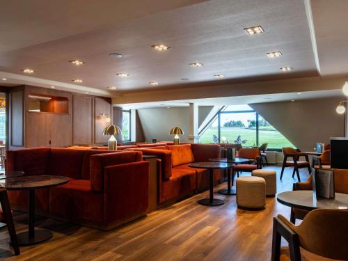 a restaurant with couches and tables and a large window at Mercure Bayeux Omaha Beach in Port-en-Bessin-Huppain