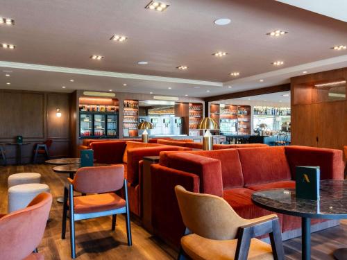 a restaurant with red chairs and tables and a bar at Mercure Bayeux Omaha Beach in Port-en-Bessin-Huppain