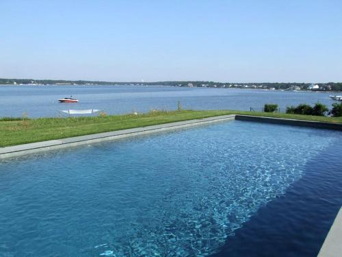 a swimming pool next to a large body of water at Stunning Waterfront Villa Rental with a Jacuzzi and a Heated Pool for a Luxury Getaway in the Hamptons, New York in Art Village