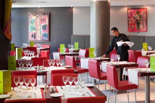 a man standing in a dining room with tables and chairs at Mercure Port La Grande Motte in La Grande-Motte