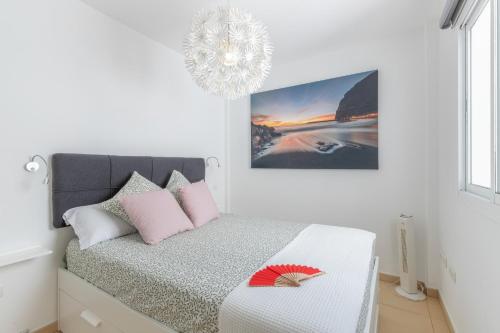a white bedroom with a bed with pink pillows and a chandelier at Apartamento Calas in Puerto Naos