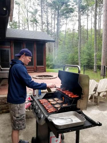 a man is cooking hot dogs on a grill at Log Cabin Elegance: Your Private Haven on 5 Acres of Hazelhurst Waterfront in Hazelhurst