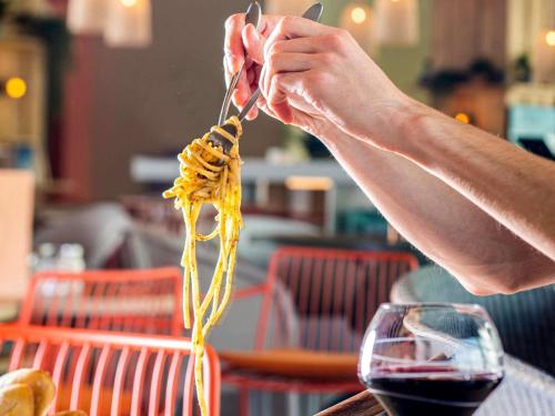 a person is holding a bunch of pasta and a glass of wine at Mercure Paris Orly Airport in Orly