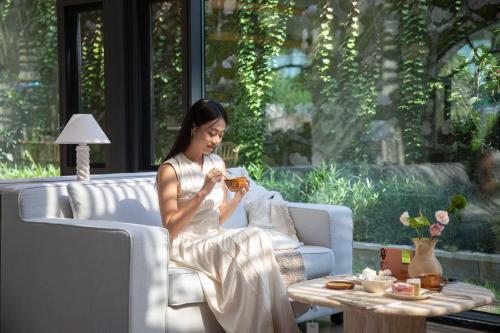 a woman sitting on a couch reading a book at Trip.com Group Country Retreats(Guangzhou Bella vita manor) in Huadong