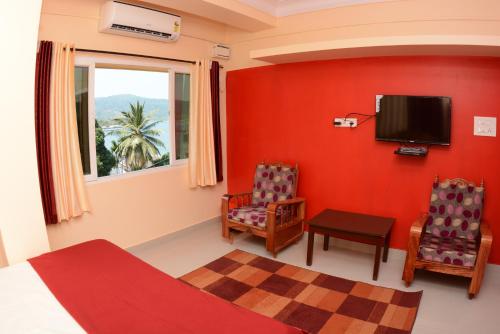 a bedroom with a red wall with a tv and two chairs at The Seaview Residency in Port Blair