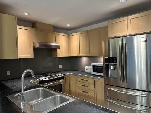 Modern 3-Bedroom Apartment in UBC في فانكوفر: مطبخ مع خزائن خشبية وثلاجة من الفولاذ المقاوم للصدأ