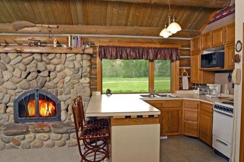 a kitchen with a stone fireplace in a log cabin at Rocky Mountains Nature Escape: Amazing Log Cabin with a Hot Tub in Darby, MT in Peaks and Pines Park