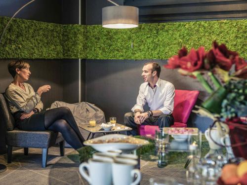 a man and woman sitting in chairs in a room at Mercure Mulhouse Centre in Mulhouse