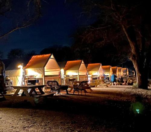 a row of tents with tables and chairs at night at 24 Son's Secluded Safari Tent in Kingsbury, TX in Staples