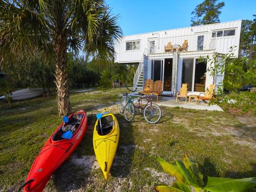 two kayaks parked next to a house with a palm tree at Upcycled Shipping Containers Transformed into a Glamping Home for a Unique Florida Vacation in Tequesta