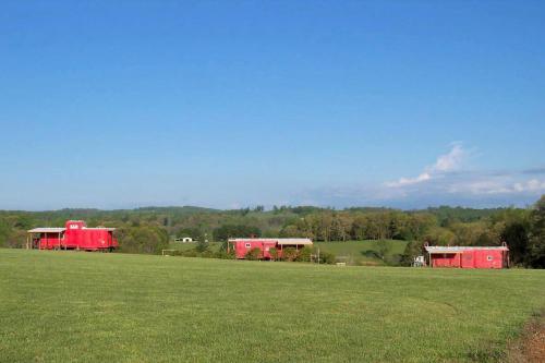 a field with two red buildings in a field at Gorgeous Caboose Rental for a Glamping Getaway in the Blue Ridge Mountains of Virginia in Laurel Fork