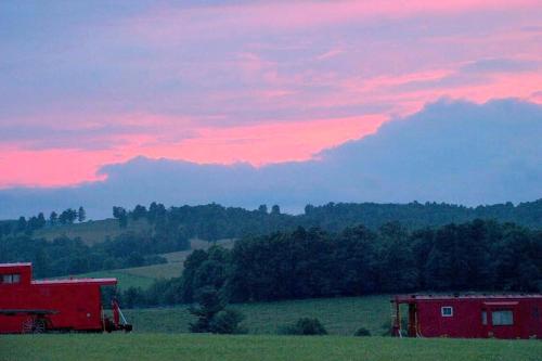 a red barn in a field with a sunset at Gorgeous Caboose Rental for a Glamping Getaway in the Blue Ridge Mountains of Virginia in Laurel Fork