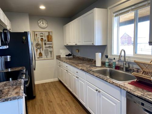 a kitchen with white cabinets and a black refrigerator at Secluded Modern Vacation Home with Madison Range Views near Ennis Lake, McAllister Montana in Ennis