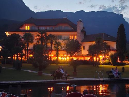 a large building with people sitting on benches near a pond at Seegarten in Caldaro