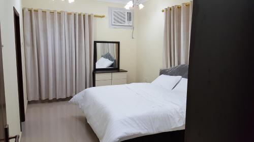 a bedroom with a white bed and a mirror at Golden Seasons Furnished Apartment - 2 in Salalah