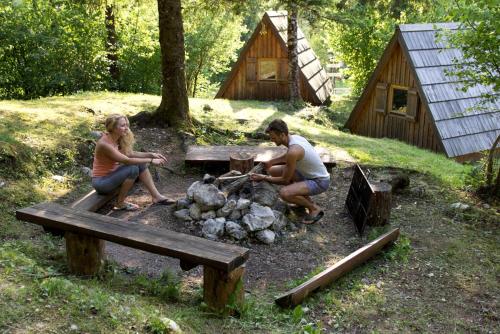 a man and woman sitting around a picnic table next to a fire at Unique A-Frame Cabin Rentals for a Vacation near Bovec, Slovenia in Soča