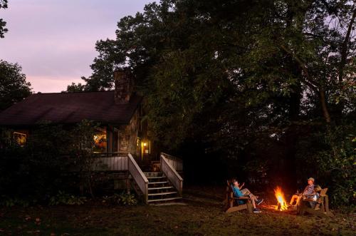 two people sitting around a fire in front of a cabin at Riverfront Cabin Rental with a Private Beach on Youghiogheny River near Pittsburgh, Pennsylvania in Confluence