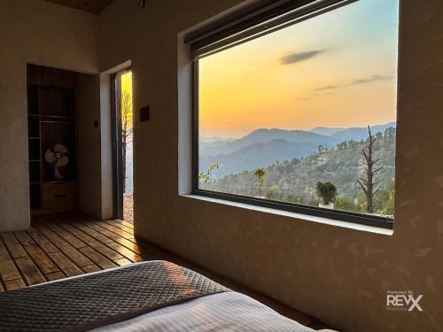 a bedroom with a large window with a mountain view at Anupraas Resort in Lansdowne