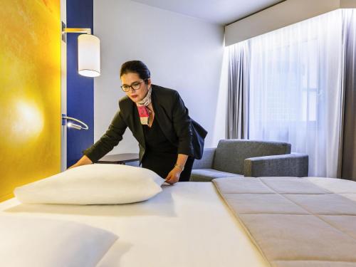 a man in a hotel room making a pillow on a bed at Mercure Rouen Centre Cathédrale in Rouen