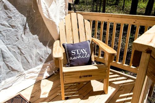 a wooden chair with a pillow sitting on a porch at Luxurious Safari Tent in Cooperstown, NY - Perfect Glamping Spot for a Romantic Getaway in Cooperstown