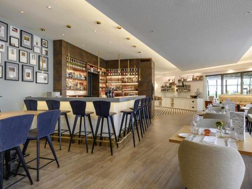 a restaurant with a bar with blue bar stools at Mercure Hotel Saarbrücken City in Saarbrücken