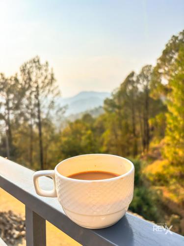 a cup of coffee sitting on a railing with a view at Anupraas Resort in Lansdowne
