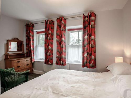 a bedroom with a bed and two windows with red curtains at 2 Bed in Aberdovey 80399 in Llwyngwril